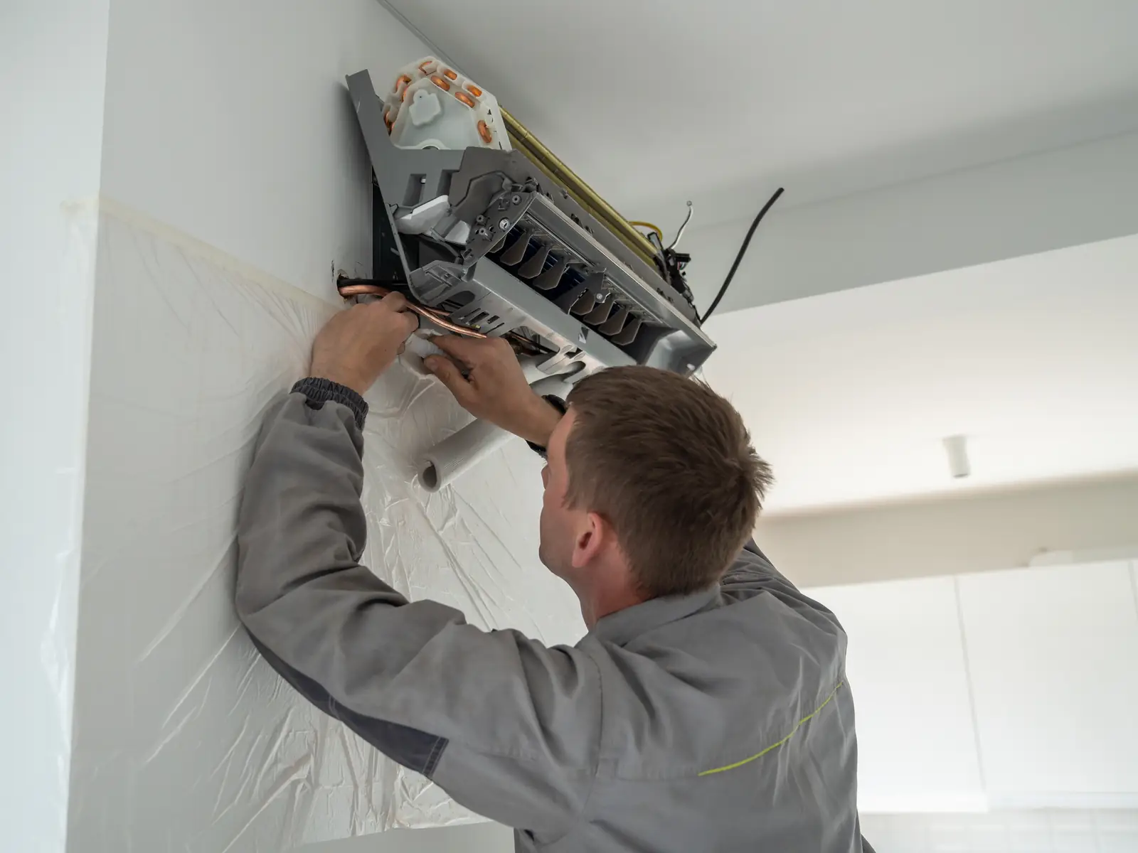 Installateur fixant un split mural lors de la pose d'une climatisation dans une maison