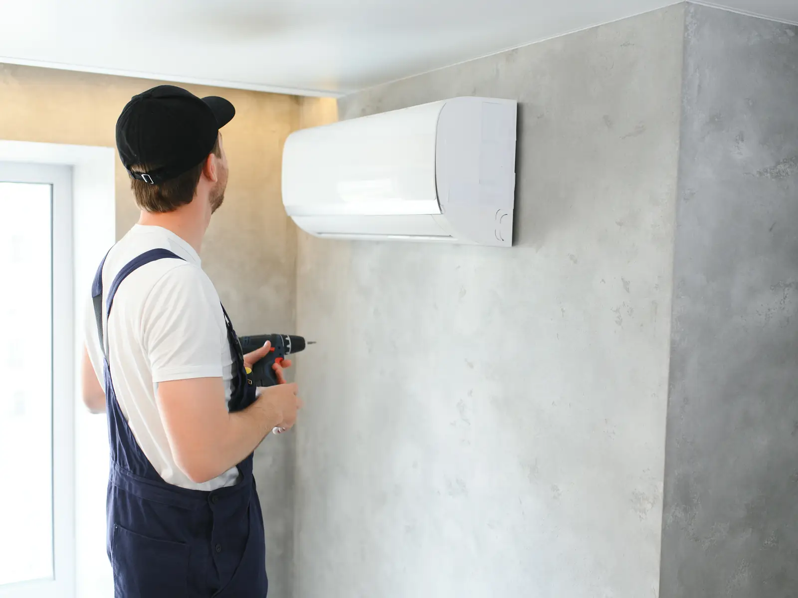 Technicien fixant une unité intérieure de climatisation murale